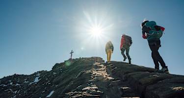 Drei Wanderer steigen auf felsigem Untergrund in Richtung Gipfelkreuz des Großen Wiesbachhorns