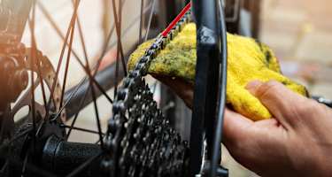 Hand die mit rotem Schlauch und gelbem Lappen eine Fahrradkette schmiert