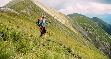 Wanderin geht mit Wanderstöcken über begrasten Berg