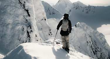 Ein Freerider steht auf einem Hang und blickt den verschneiten Berg hinab.