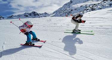 Eine Frau und ein Mädchen fahren gemeinsam Ski und nehmen dabei die Schussposition ein.