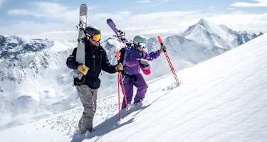 Ein Skifahrer und eine Skifahrerin gehen eine Piste in Ischgl hinauf.