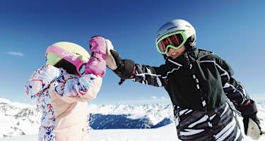 Ein Mädchen und ein Junge geben sich ein High Five. Hinter ihnen erstreckt sich das Bergpanorama von Kappl.