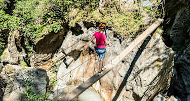 Mädchen im Klettersteigset beim Balancieren auf einem Baumstamm in der Feeschlucht