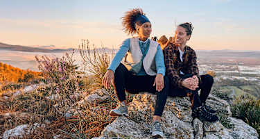 Zwei Frauen sitzen auf einem Fels in den Bergen.