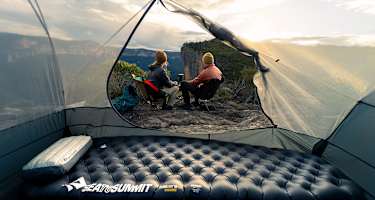 Sea to Summit Isomatte und Kissen im Zelt mit Blick auf zwei Camper, die den Sonnenuntergang in den Bergen genießen