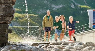 Eine Familie läuft einem plätscherndem Wasserstrahl entgegen.