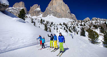 Fünf Skifahrer fahren die Sellaronda in Südtirol im Hintergrund ein schönes Dolomitenpanorama.