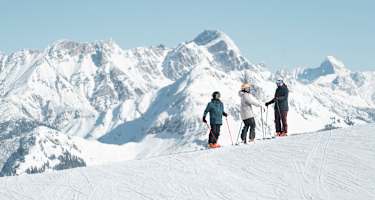 Drei Skifahrer sind im Skicircus Saalbach Hinterglemm Leogang Fieberbrunn unterwegs und blicken in die Kamera. Im Hintergrund sieht man eine verschneite Berglandschaft.