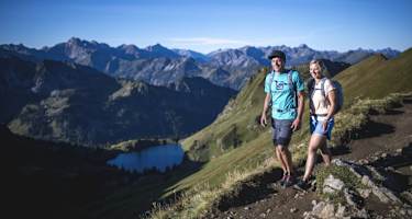 Zwei Wanderer vor einer schönen Berglandschaft mit einem blauen See.