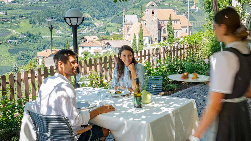 Ein Pärchen sitzt auf der Terrasse eines Restaurants in Schenna und bekommt typische Südtiroler Spezialitäten serviert.