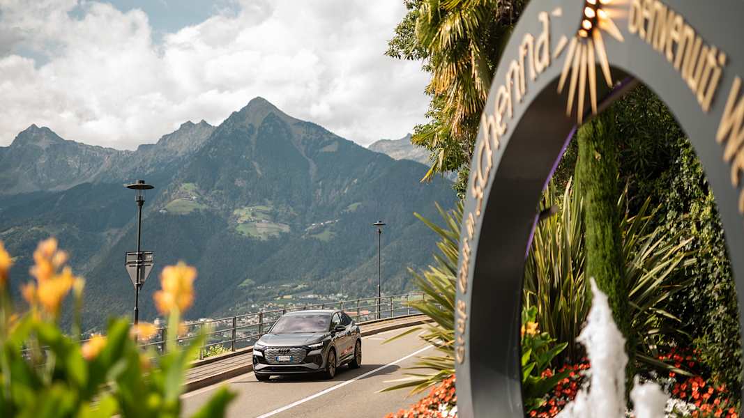Ein modernes Auto auf der Straße, die nach Schenna führt, im Hintergrund die Bergwelt.