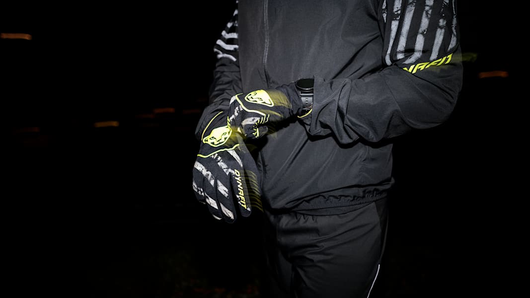 Ein Mann trägt schwarze Handschuhe mit Neon-Elementen von DYNAFIT.