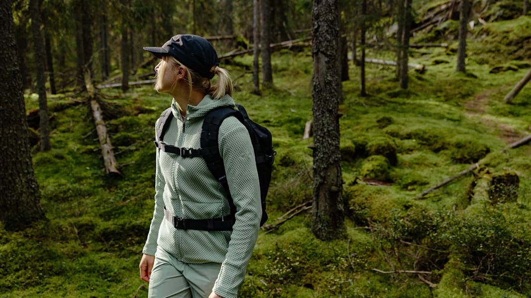 Frau im grünen Wald mit Kappe und türkiser Kleidung.