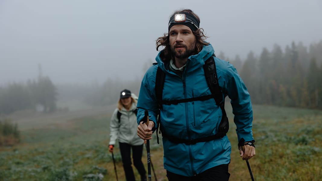 ein Mann und eine Frau beim Wandern im Wald mit Stirnlampen.
