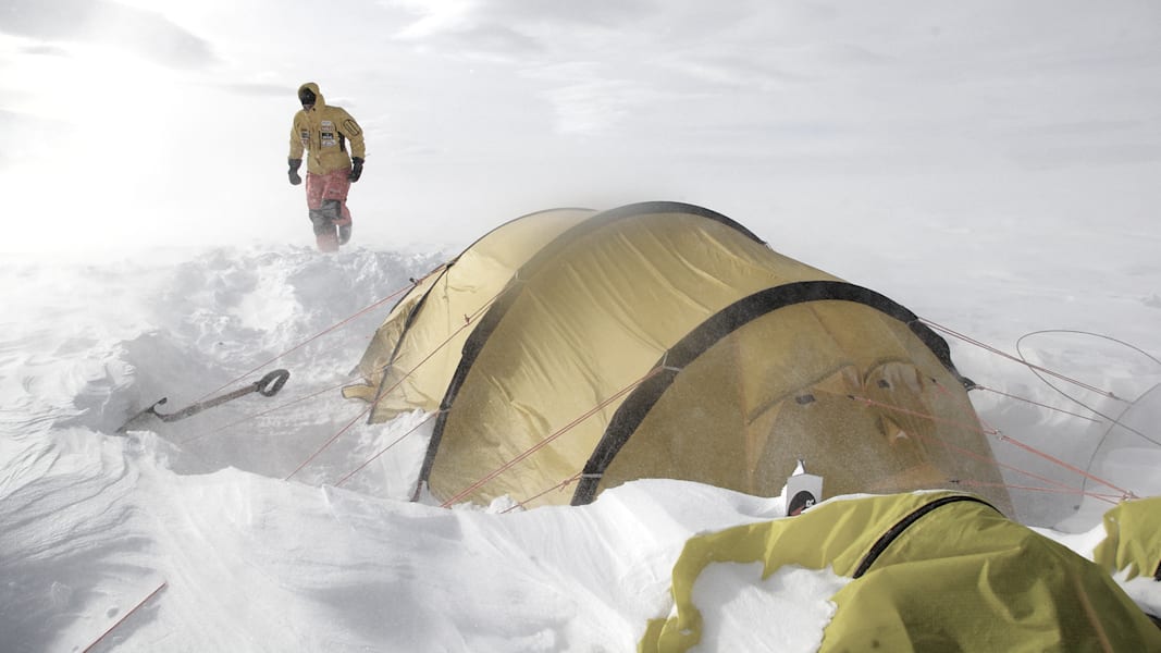 Ein Mann stapft durch Schnee und Eis zu seinem Zelt.