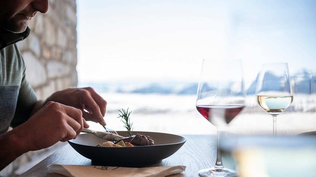 Mann isst genüsslich Wild mit Blick auf Berge