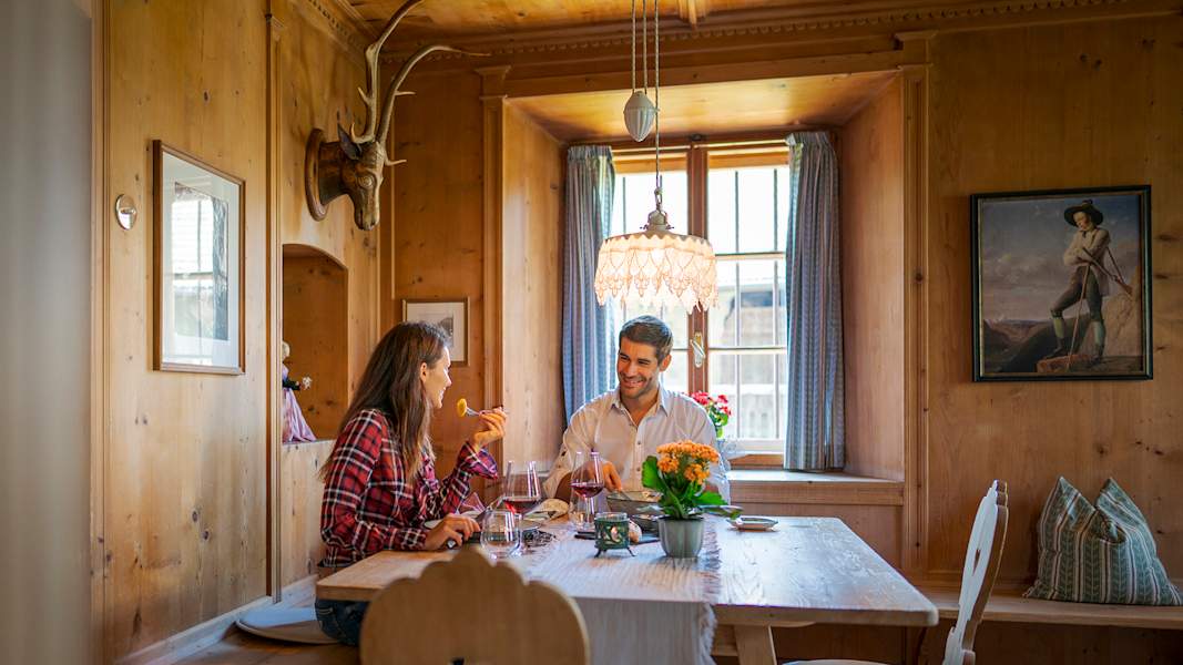 Paar sitzt in einer urigen Hütte und genießt ein Glas Wein und gutes Essen in Schenna
