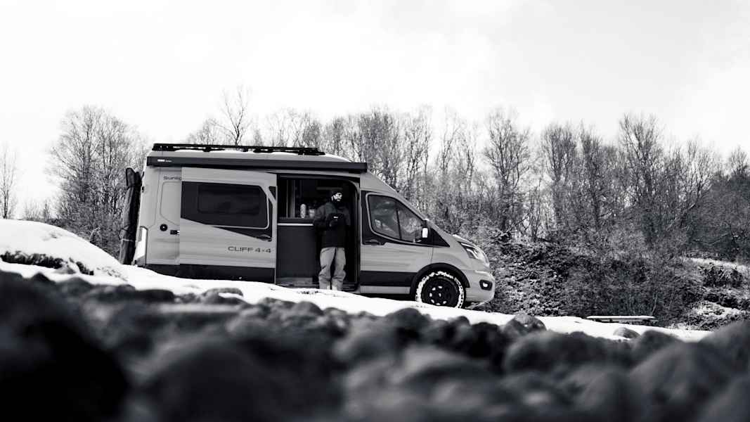 Ein Campervan steht in einer verschneiten Landschaft, umgeben von kahlen Bäumen, ideal für Abenteuer in Nord-Norwegen.