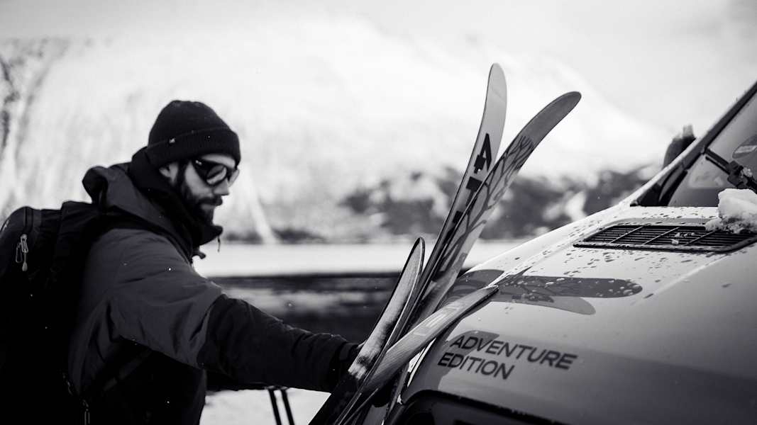 Person lädt Skier auf einen Camper vor schneebedeckter Bergkulisse in Nord-Norwegen.