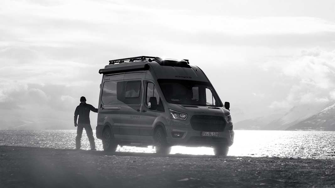 Campervan steht am Ufer eines Fjords in Nord-Norwegen, umgeben von Bergen und winterlicher Landschaft.