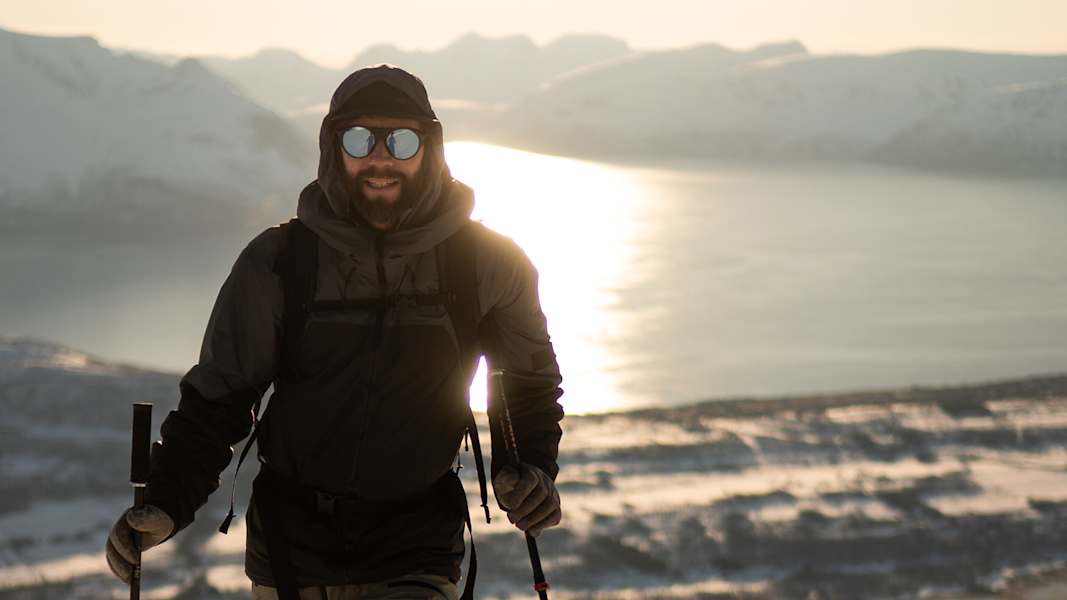 Skitourengeher in winterlicher Landschaft mit Blick auf einen Fjord, beleuchtet von der tiefstehenden Sonne in Nord-Norwegen.