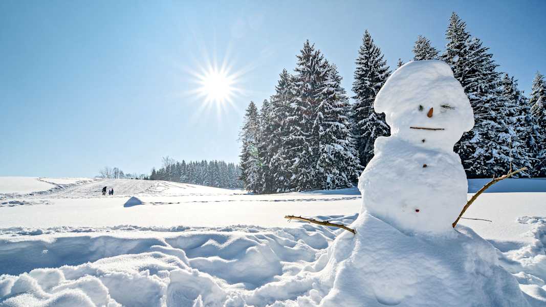 Ein Schneemann steht vor einer sonnigen Winterlandschaft.
