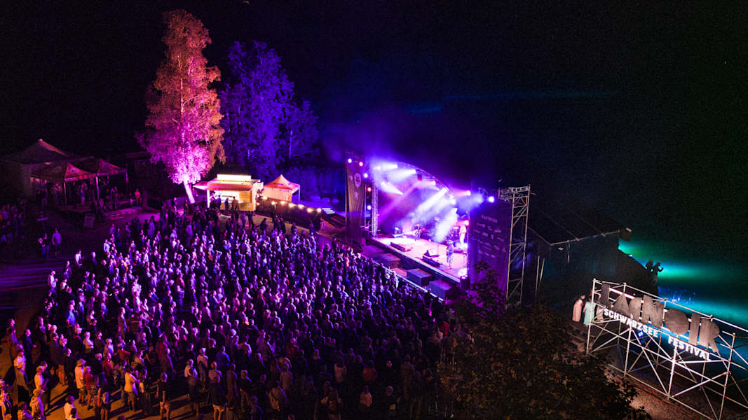 Eine Open Air-Bühne mit einer tanzenden Menschenmenge am Schwarzsee mit einer bunten Lichtershow.