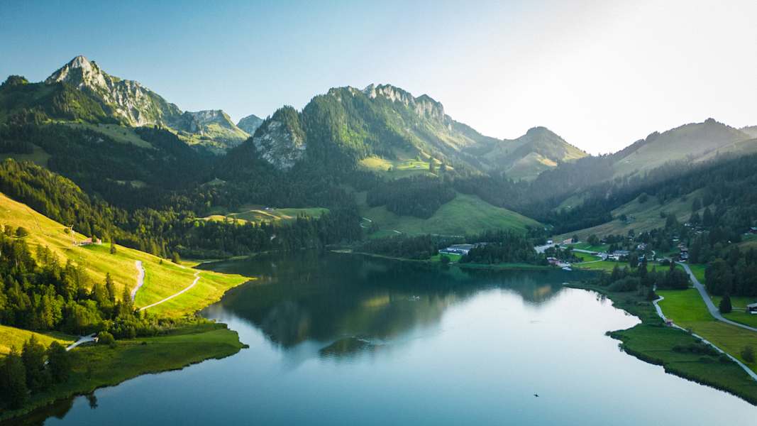 Idyllisch liegt der dunkle Schwarzsee zwischen grünen Almwiesen und grauen Bergen.