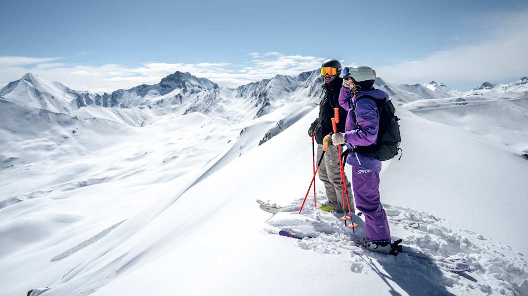 Ein Skifahrer und eine Skifahrerin stehen auf einem Berg und genießen das schneereiche Panorama im Paznaun.