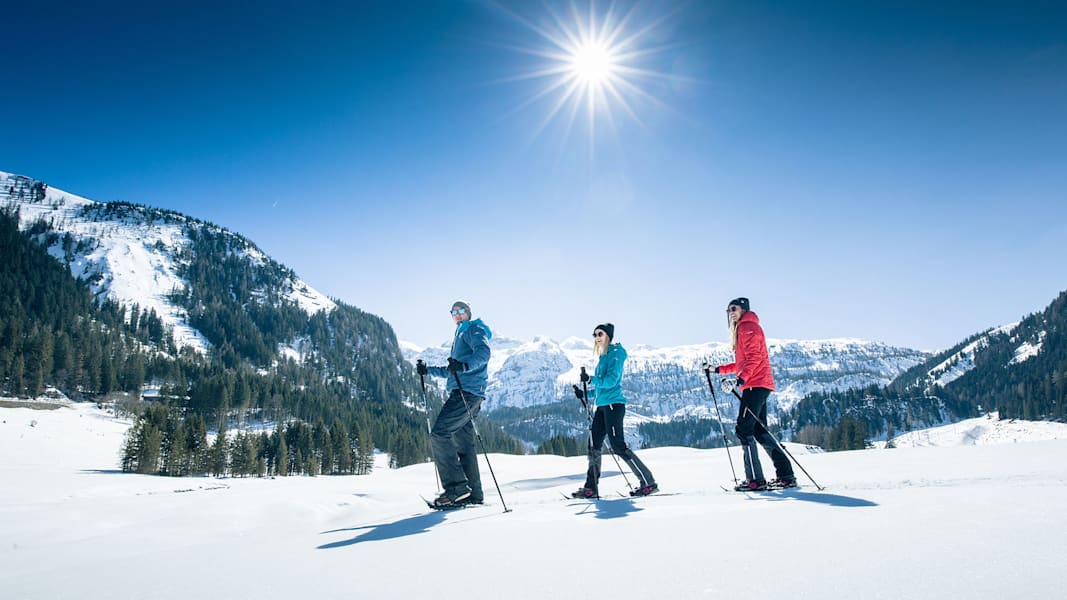 Drei Winterwanderer gehen durch die verschneite Winterlandschaft, während die Sonne scheint.