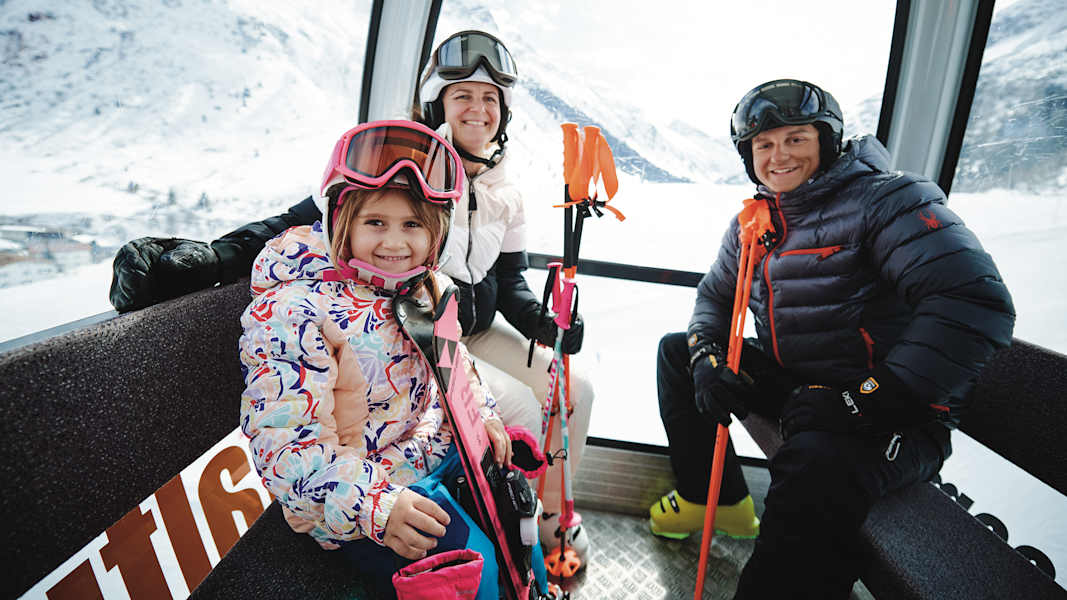 In einer Gondel sitzt eine dreiköpfige Familie in voller Skimontur.