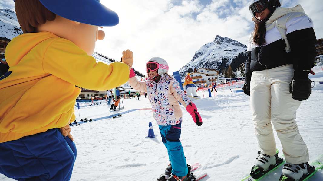 Ein Mädchen gibt dem Maskottchen des Skigebiets ein High-Five.