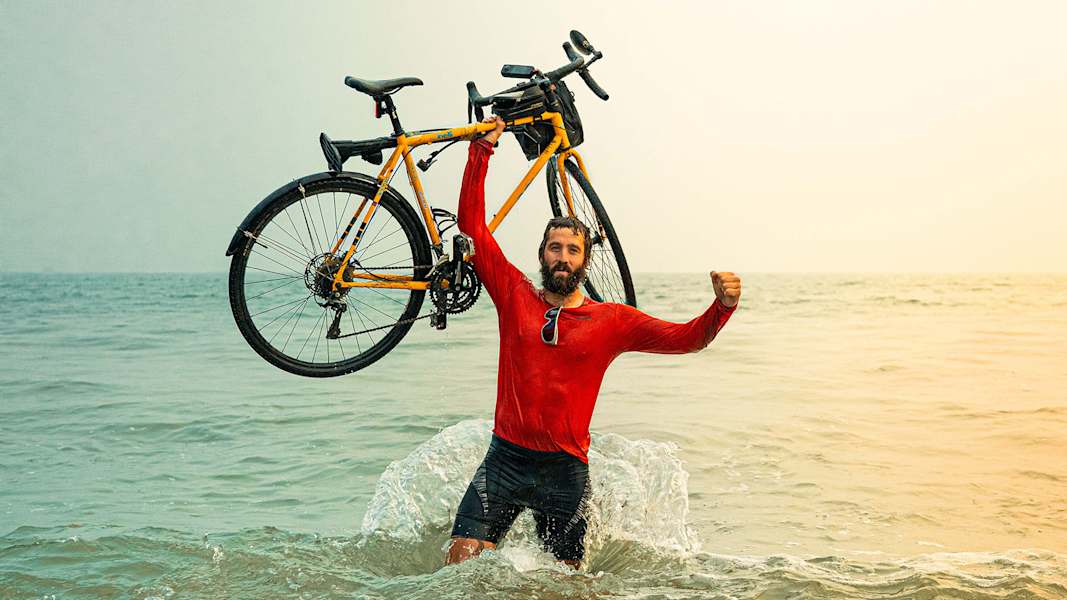 Stolz hält Mitchell Hutchcraft sein Rad hoch, während er im Meer steht.