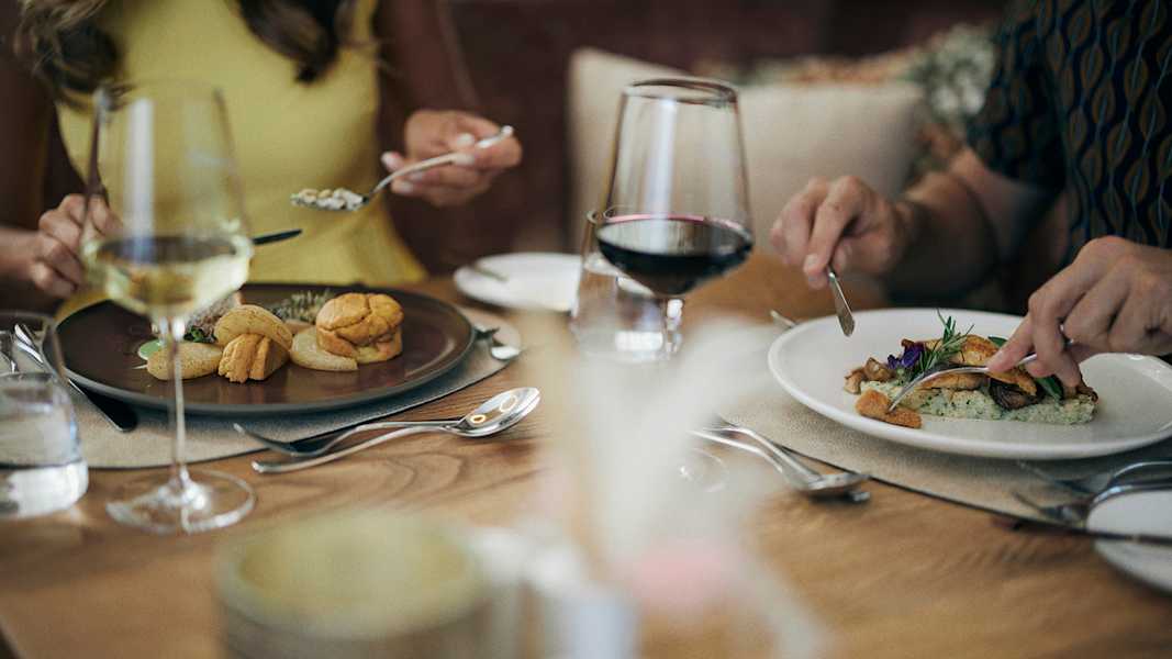 Zwei Personen sitzen an einem gedeckten Tisch, genießen ein Abendessen mit Wein und feinen Speisen im Hotel Guglwald.