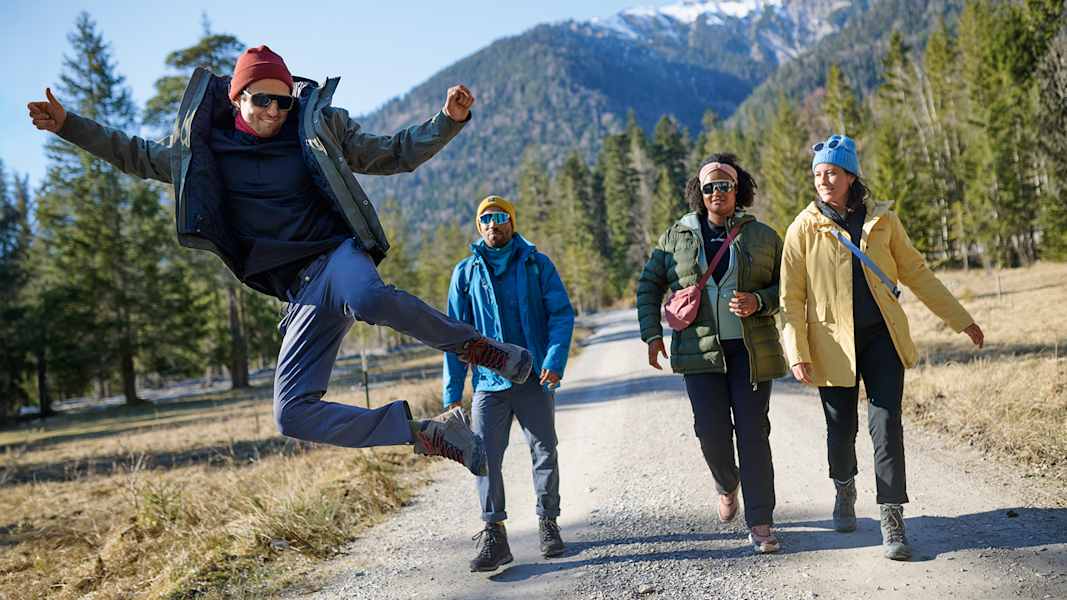 Gruppe von Wanderern in funktionaler Outdoorbekleidung von Maier Sports auf einem Waldweg, umgeben von Bergen und Natur.