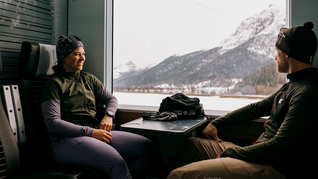 Ein Paar sitzt im Zug mit Bergpanorama und lächelt sich an.