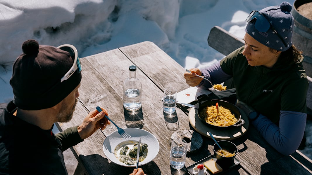 Ein Mann und eine Frau sitzen draussen im Winter bei einem Gasthaus und essen Spezialitäten aus der Schweiz.