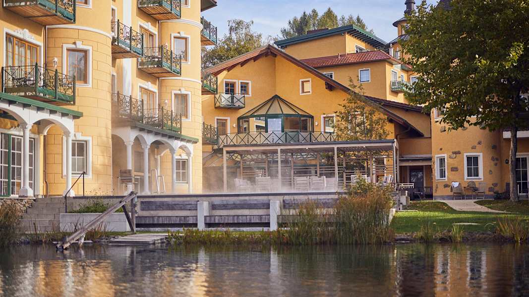 Außenansicht des Hotel Guglwald mit See und Garten im Vordergrund, umgeben von herbstlicher Natur im Böhmerwald.