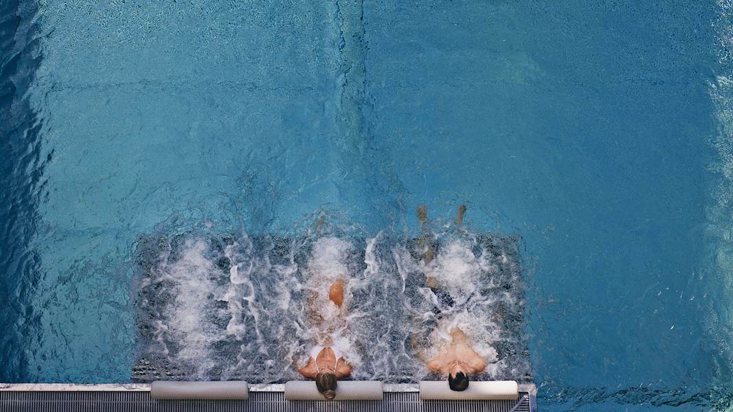 Zwei Personen liegen nebeneinander auf Liegen im Pools vom Hotel Guglwald und genießen die Ruhe am Wasser.
