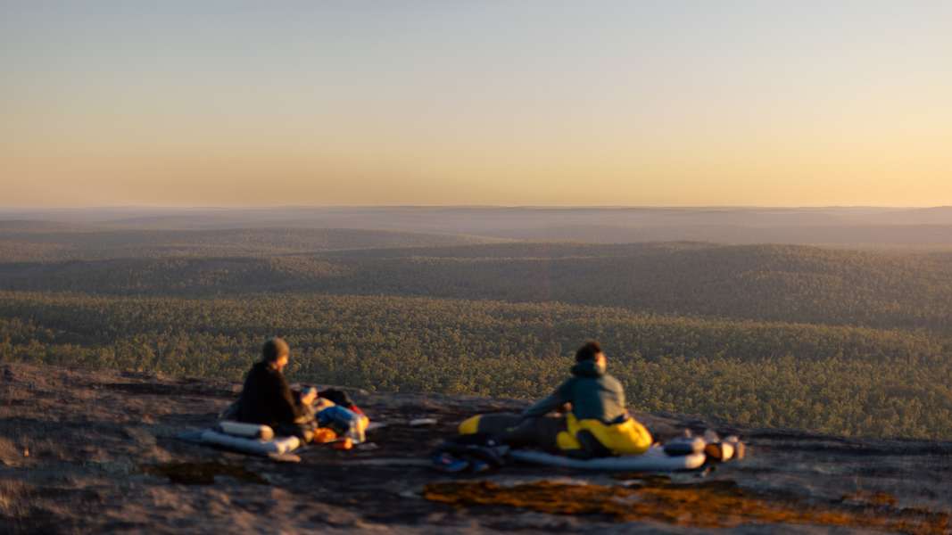 Zwei Camper mit Sea to Summit Ausrüstung genießen den Sonnenaufgang über einem weiten Waldpanorama