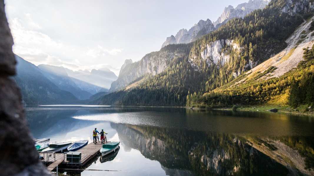 Zwei Biker auf einem Steg am Gosausee, im Hintergrund der Dachstein.