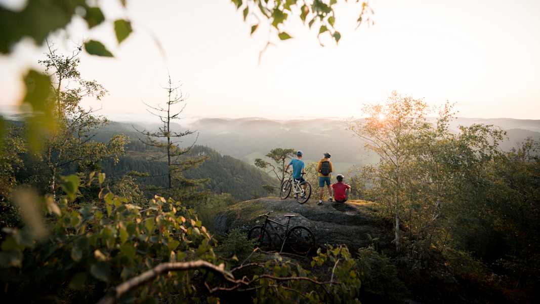 Drei Mountainbiker sitzen auf einem Fels und schauen in die Ferne.