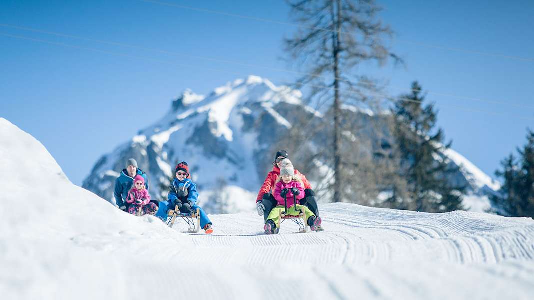 Eltern rodeln mit ihren Kindern eine präperierte Piste hinab.