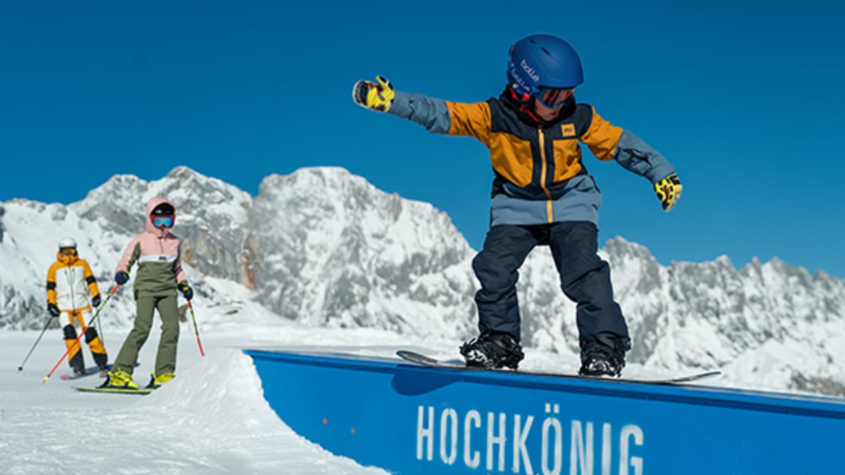 Ein kleiner Junge macht mit dem Snowboard auf der Piste Tricks.