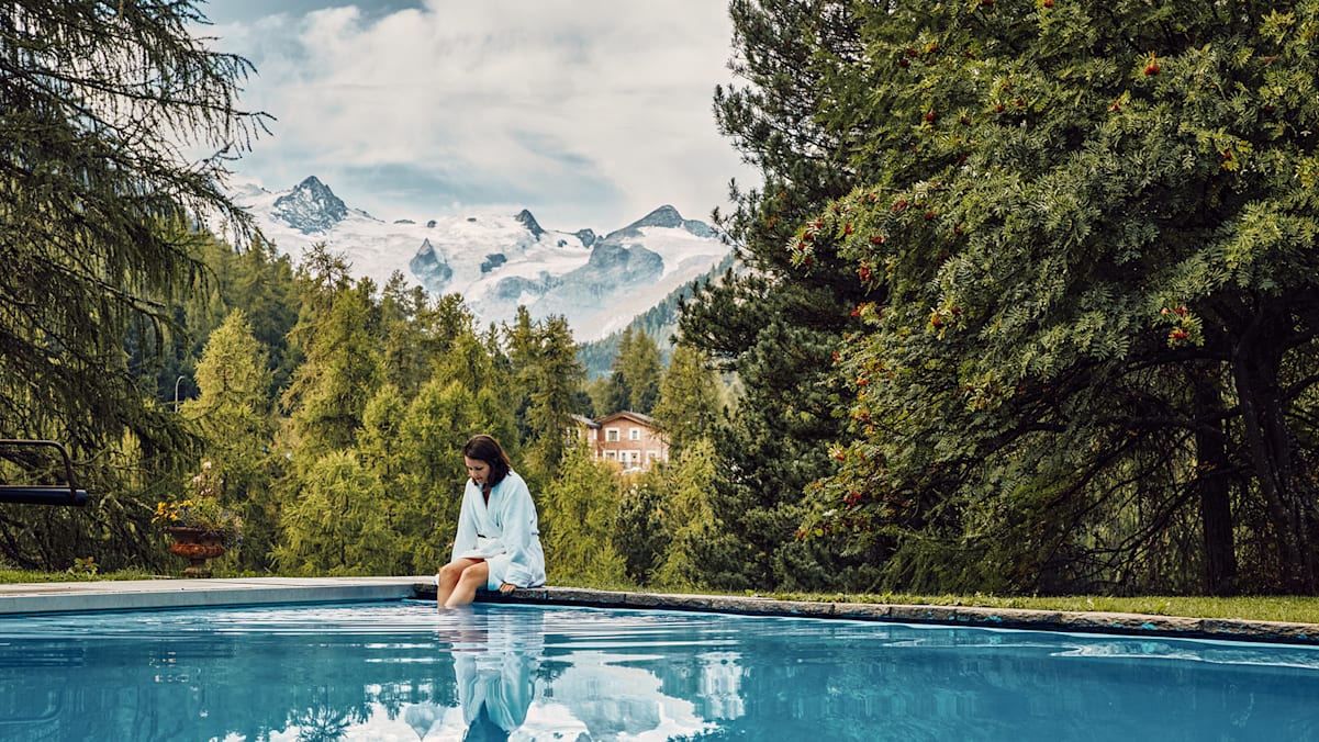 Eine Frau am Pool umgeben von Bergen und Bäumen in der Schweiz.