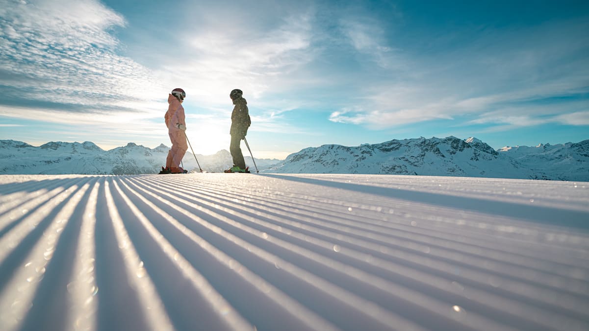 Zwei Skifahrer stehen mit Ausrüstung auf einer frisch präparierten Piste.