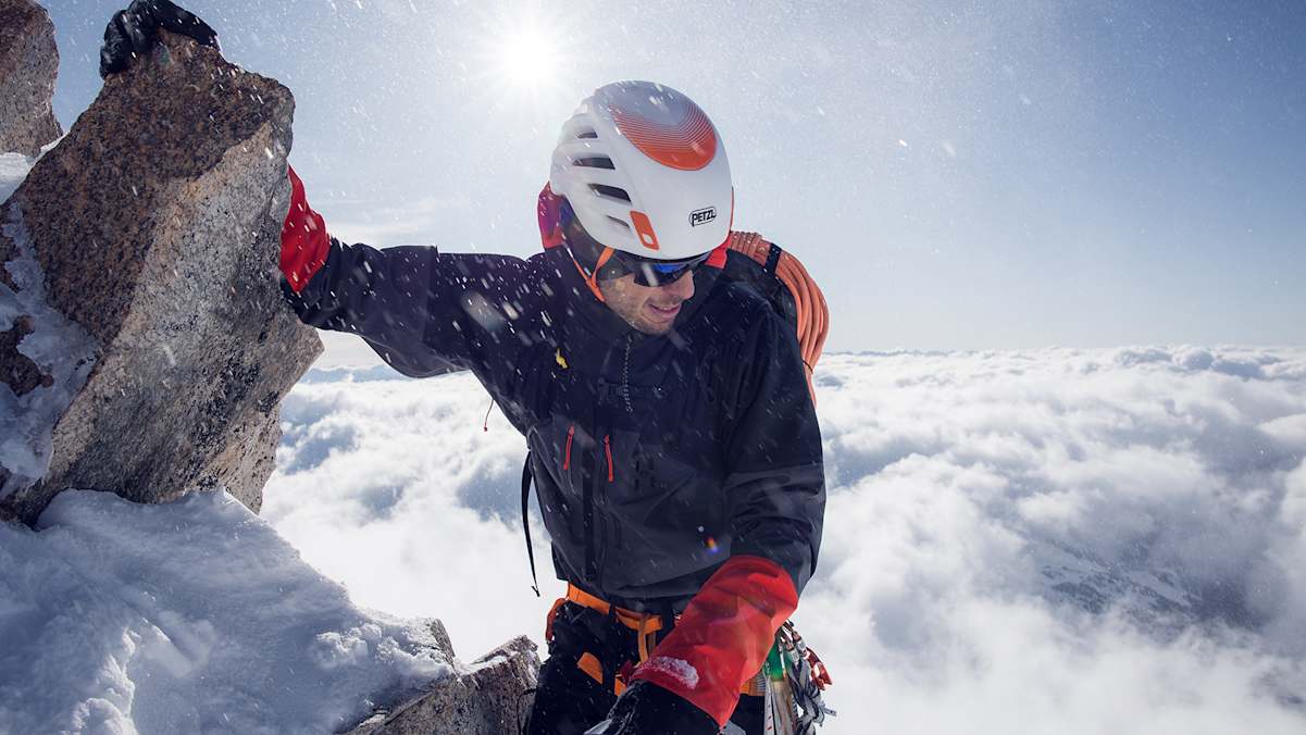 mann beim bergsteigen auf bergspitze, gekleidet in haglöfs