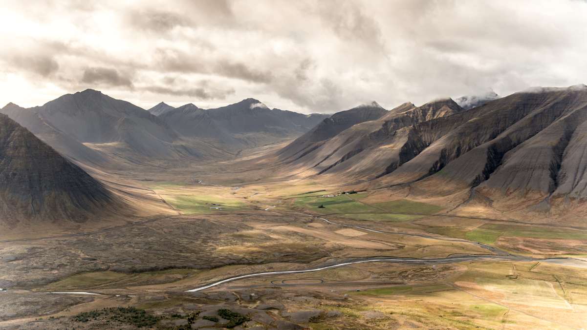 Wenig besiedelte Berge unter bewölktem Himmel und landwirtschaftlichen Flächen