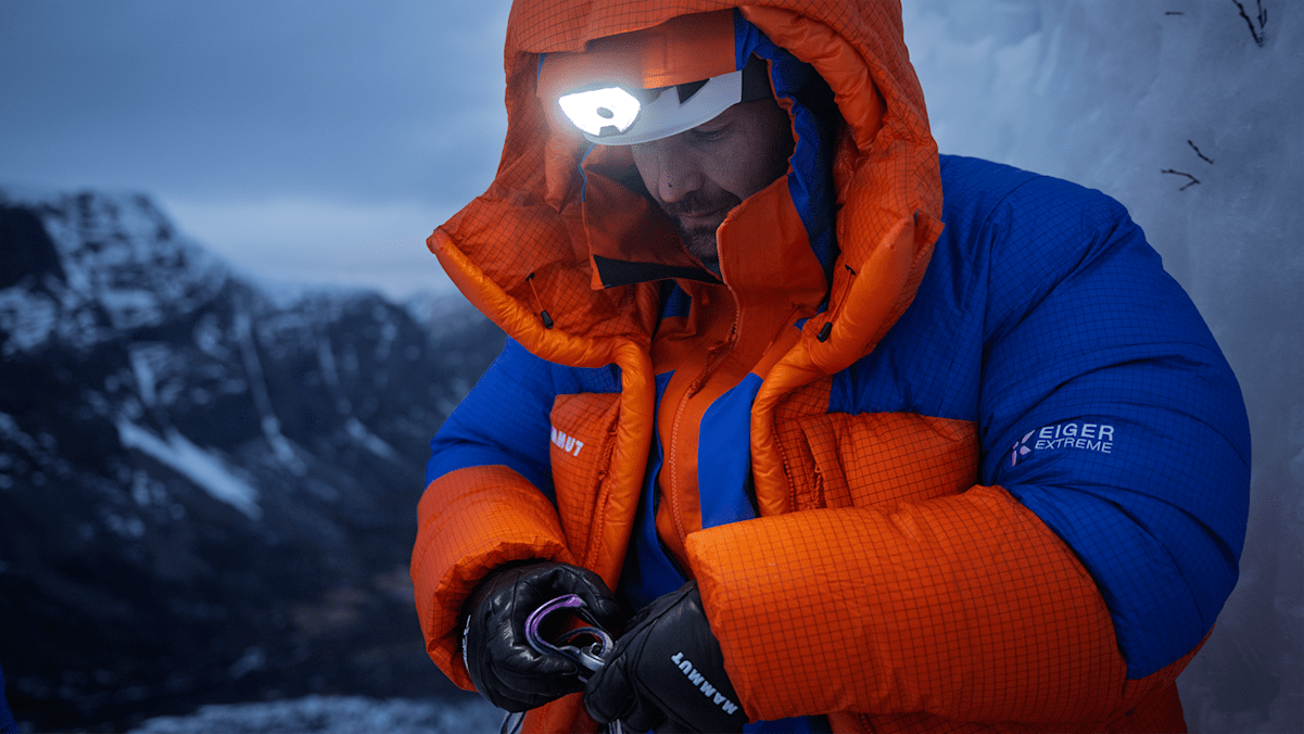 Ein Alpinist steht in den schneebedeckten Bergen und ist mit der neuen Eiger Extreme Nordwand 6.0 Kollektion von Mammut ausgestattet. Über seinem Helm trägt er eine Stirnlampe.